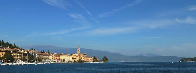 Trip Deutschland beliebte Urlaubsziele am Gardasee -  Mit einer Fläche von 370 km² ist der Gardasee der größte See Italiens. Es liegt am Fuße der Alpen und erstreckt sich über drei Staaten: Lombardei, Venetien und Trentino. Die maximale Tiefe des Sees beträgt 346 m, er hat eine längliche Form und sein nördliches Ende ist sehr schmal. Dort ist der See von den Bergen der Gruppo di Baldo umgeben. Du trittst aus deinem gemütlichen Hotelzimmer und es begrüßt dich die warme italienische Sonne. Du blickst auf den atemberaubenden Gardasee, der in zahlreichen Blautönen schimmert - von tiefem Dunkelblau bis zu funkelndem Türkis. Majestätische Berge umgeben dich, während die Brise sanft deine Haut streichelt und der Duft von blühenden Zitronenbäumen deine Nase kitzelt. Du schlenderst die malerischen, engen Gassen entlang, vorbei an farbenfrohen, blumengeschmückten Häusern. Vereinzelt unterbricht das fröhliche Lachen der Einheimischen die friedvolle Stille. Du fühlst dich wie in einem Traum, der nicht enden will. Jeder Schritt führt dich zu neuen Entdeckungen und Abenteuern. Du probierst die köstliche italienische Küche mit ihren frischen Zutaten und verführerischen Aromen. Die Sonne geht langsam unter und taucht den Himmel in ein leuchtendes Orange-rot - ein spektakulärer Anblick.